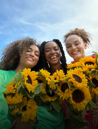 Una selfie nítida y a todo color de tres personas con flores en la mano.